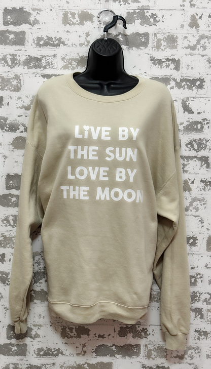 Beige sweatshirt with text 'Live by the sun, love by the moon' on a textured wall background