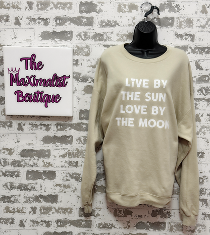 Beige sweatshirt with text 'Live by the sun, love by the moon' on a textured wall with 'The Maximalist Boutique' sign.