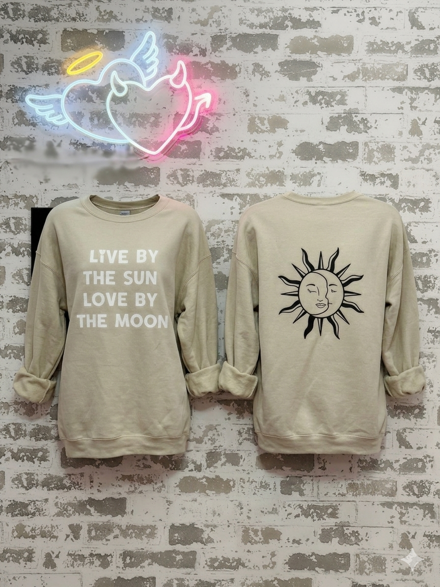 Two beige sweatshirts with text and graphics on a textured wall with a neon sign.