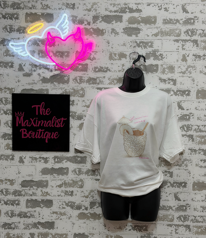 White t-shirt with graphic design on a mannequin against a textured wall with neon sign and 'The Maximalist Boutique' sign.