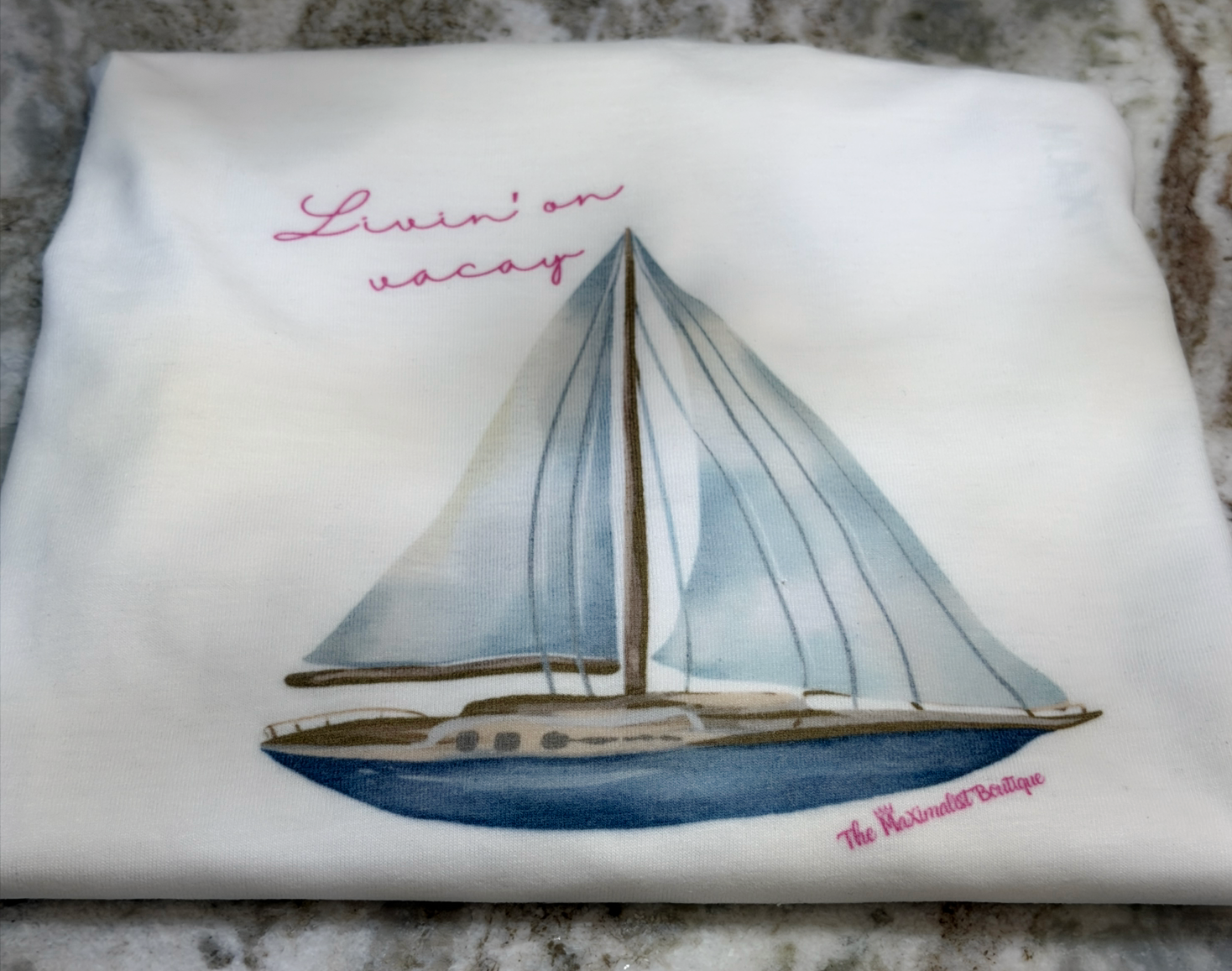 White tee with sailboat design and text on a textured surface