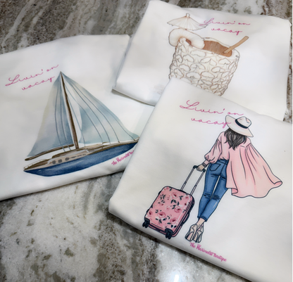 Three tees with travel-themed illustrations on a marble surface.