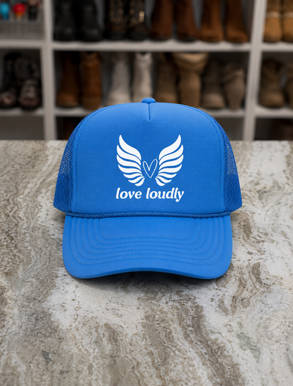 Blue cap with 'love loudly' logo on a stone surface with shoes in the background