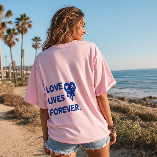 Woman wearing a pink t-shirt with 'LOVE LIVES FOREVER' text on the beach.