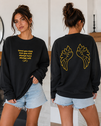Black sweatshirt with gold text and wings worn by a person indoors.