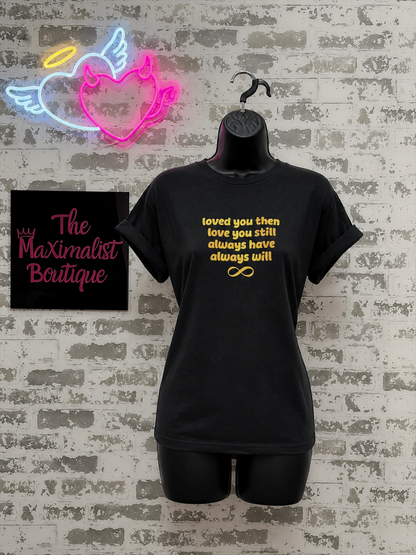 Black t-shirt with gold text on a mannequin against a brick wall with neon signs and 'The Maximalist Boutique' sign.