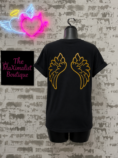 Black t-shirt with gold wings design on a textured wall with neon signs and 'The MaXimalist Boutique' sign.