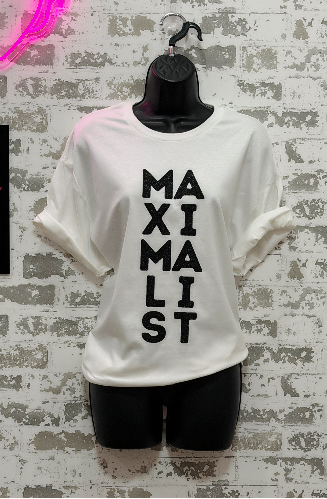 White t-shirt with 'MAXIMALIST' text on a textured wall background