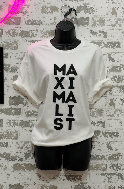 White t-shirt with 'MAXIMALIST' text on a textured wall background