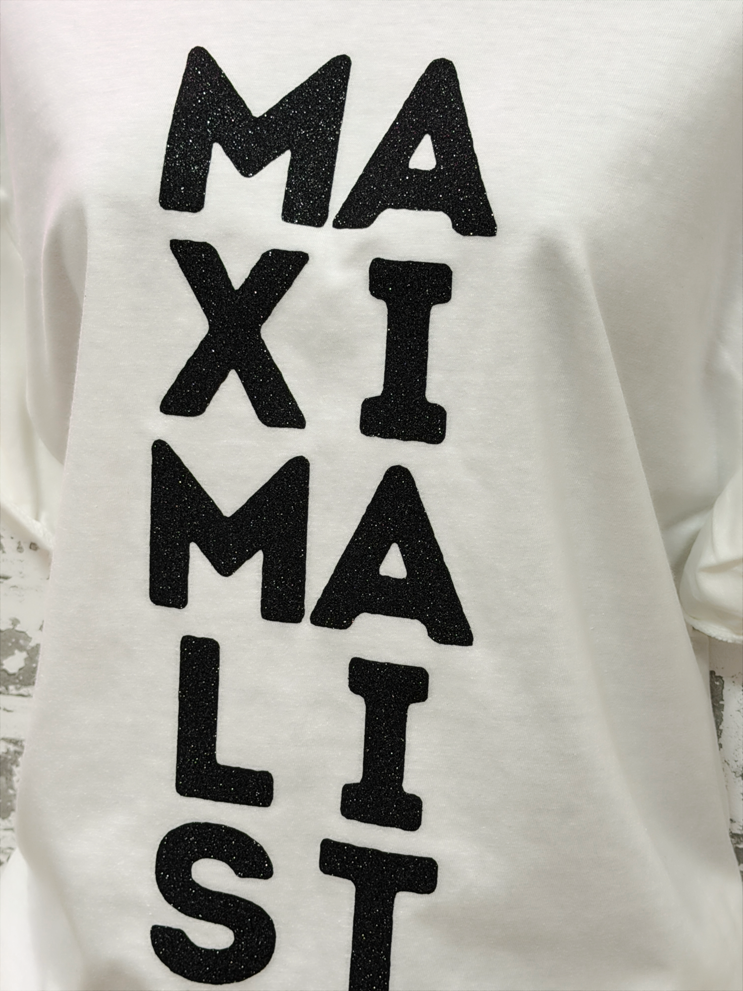 White sweatshirt with 'MAXIMALIST' text in black on a textured background