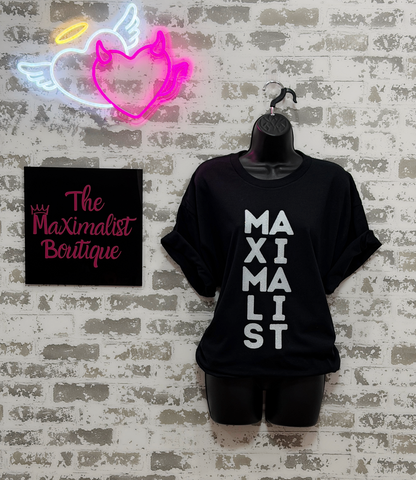 Black t-shirt with 'MAXIMALIST' text, neon sign, and 'The Maximalist Boutique' sign on a textured wall.