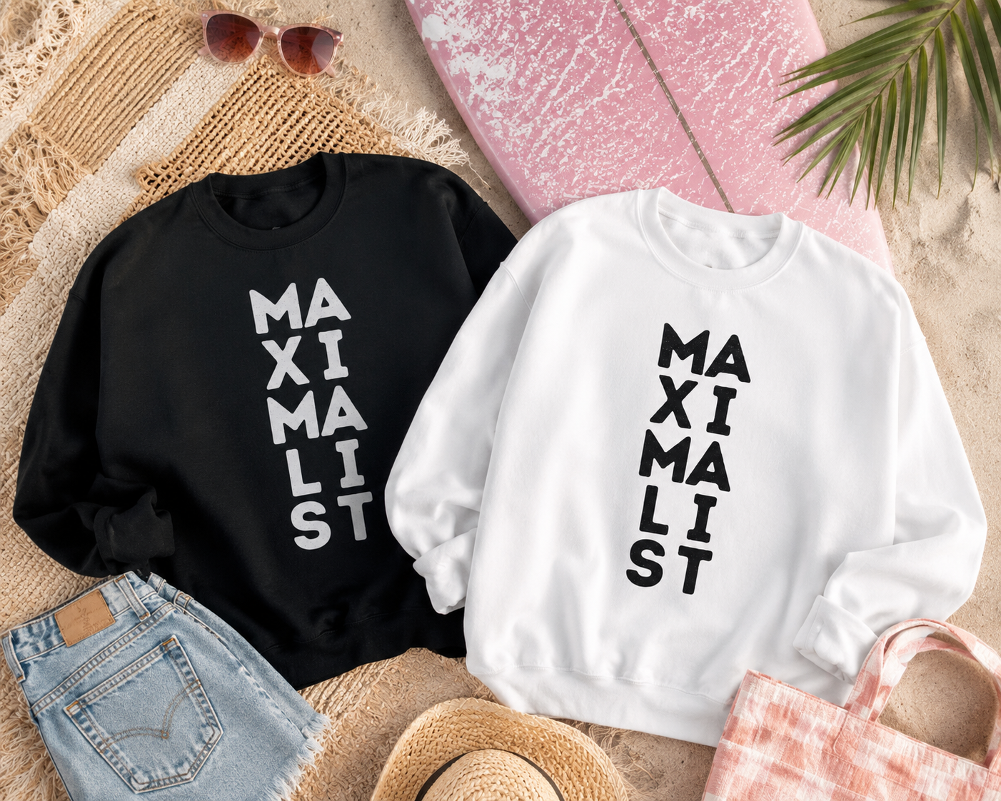 Two crewneck sweatshirts laid flat on a beach-themed background. One sweatshirt is black with the word 'MAXIMALIST' printed vertically in white, and the other is white with the same text printed vertically in black.