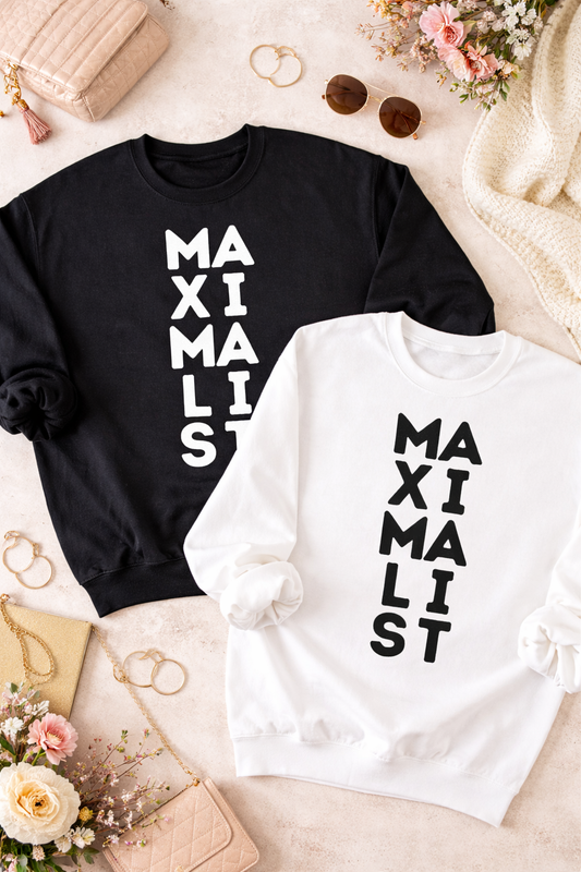 Black and white sweatshirts with 'MAXIMALIST' text on a decorative surface with flowers and jewelry.