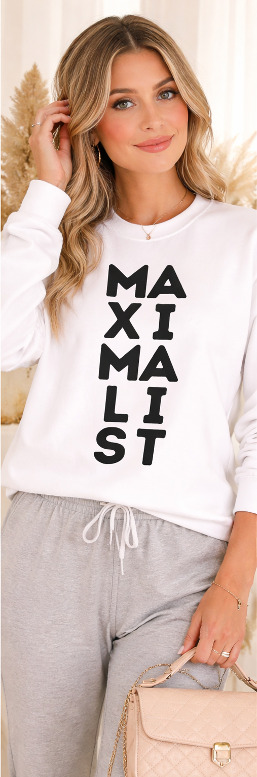 Woman wearing a white sweatshirt with 'MAXIMALIST' text, standing indoors.