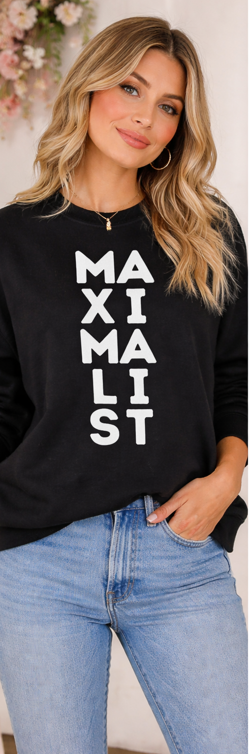 Woman wearing a black sweatshirt with 'MAXIMALIST' text, standing against a light background.