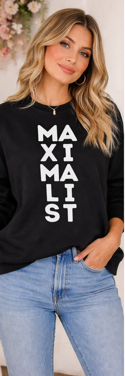 Woman wearing a black sweatshirt with 'MAXIMALIST' text, standing against a light background.