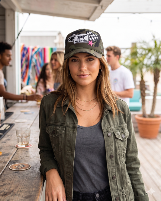 Woman wearing a cap and green jacket standing outdoors with blurred people and plants in the background