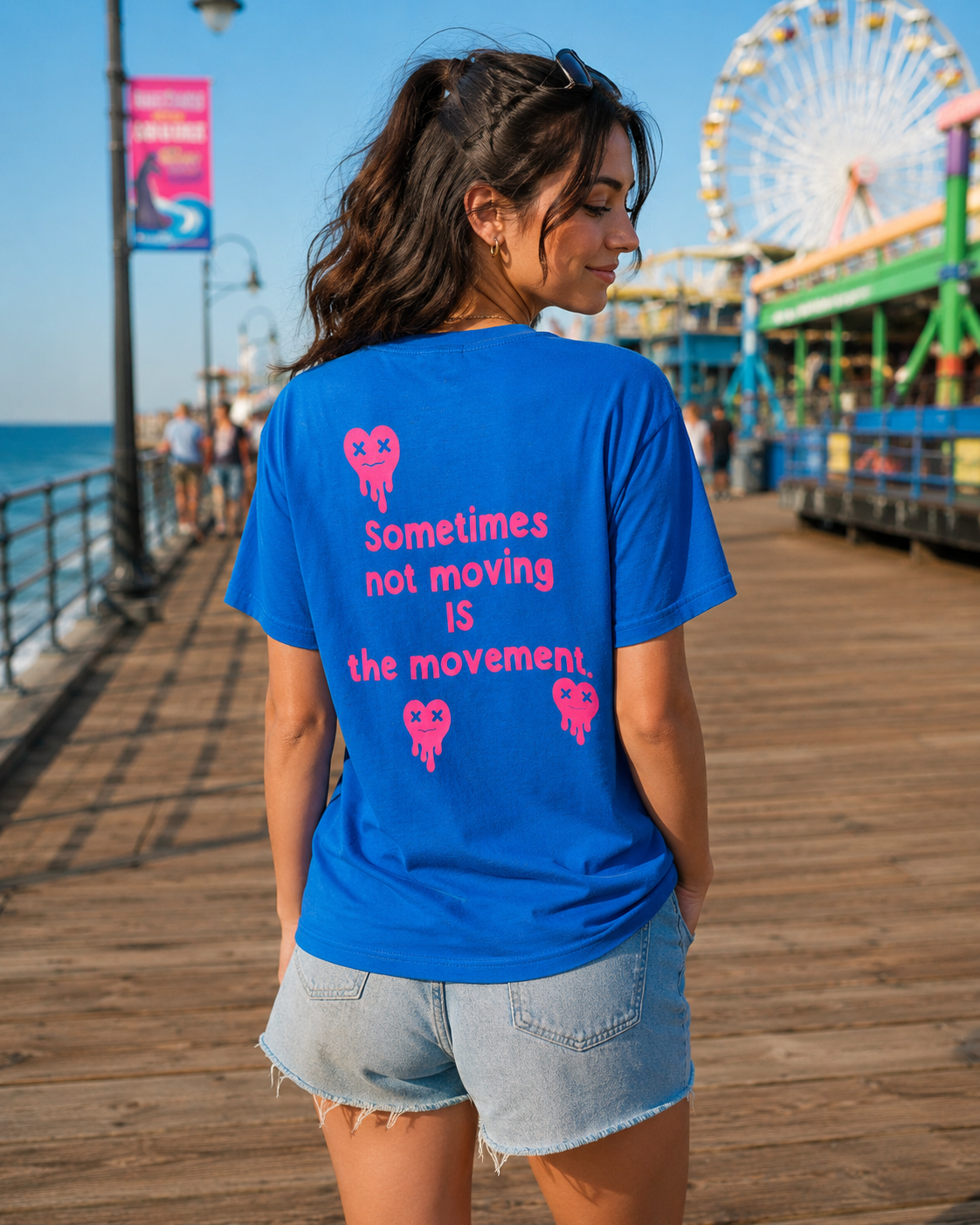 Woman wearing a blue t-shirt with a motivational quote on a pier with a Ferris wheel in the background.