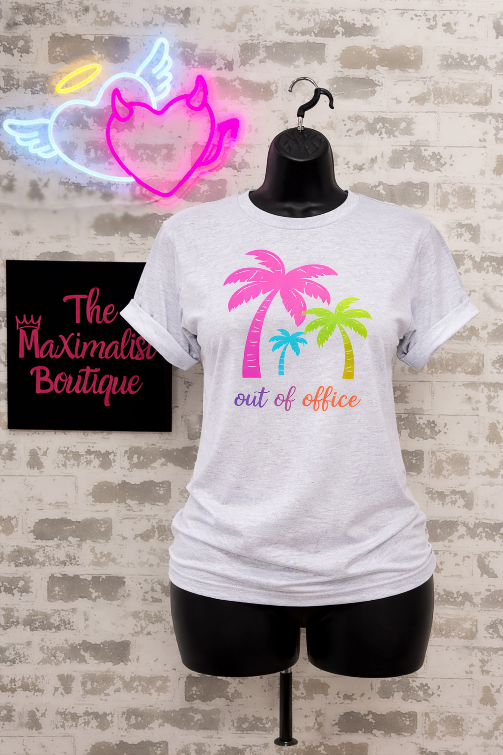 Gray t-shirt with palm tree design and text on a mannequin against a brick wall background.