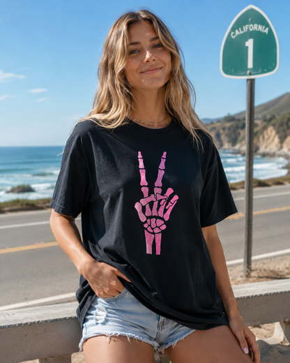 Woman wearing a black t-shirt with a pink skeleton hand design by a scenic road with ocean view.