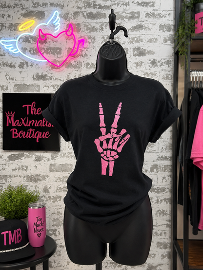 Black t-shirt with pink skeleton hand design on a mannequin against a brick wall with neon signs.