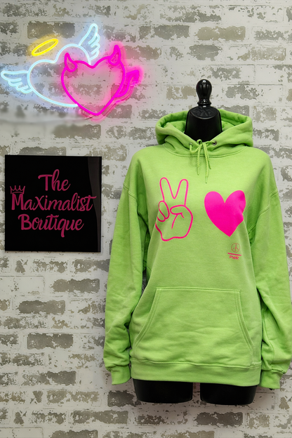 Neon green hoodie with pink peace sign and heart design on a mannequin against a brick wall with neon signs.