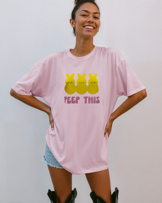 Woman wearing a pink t-shirt with yellow characters and 'PEEP THIS' text on a plain background