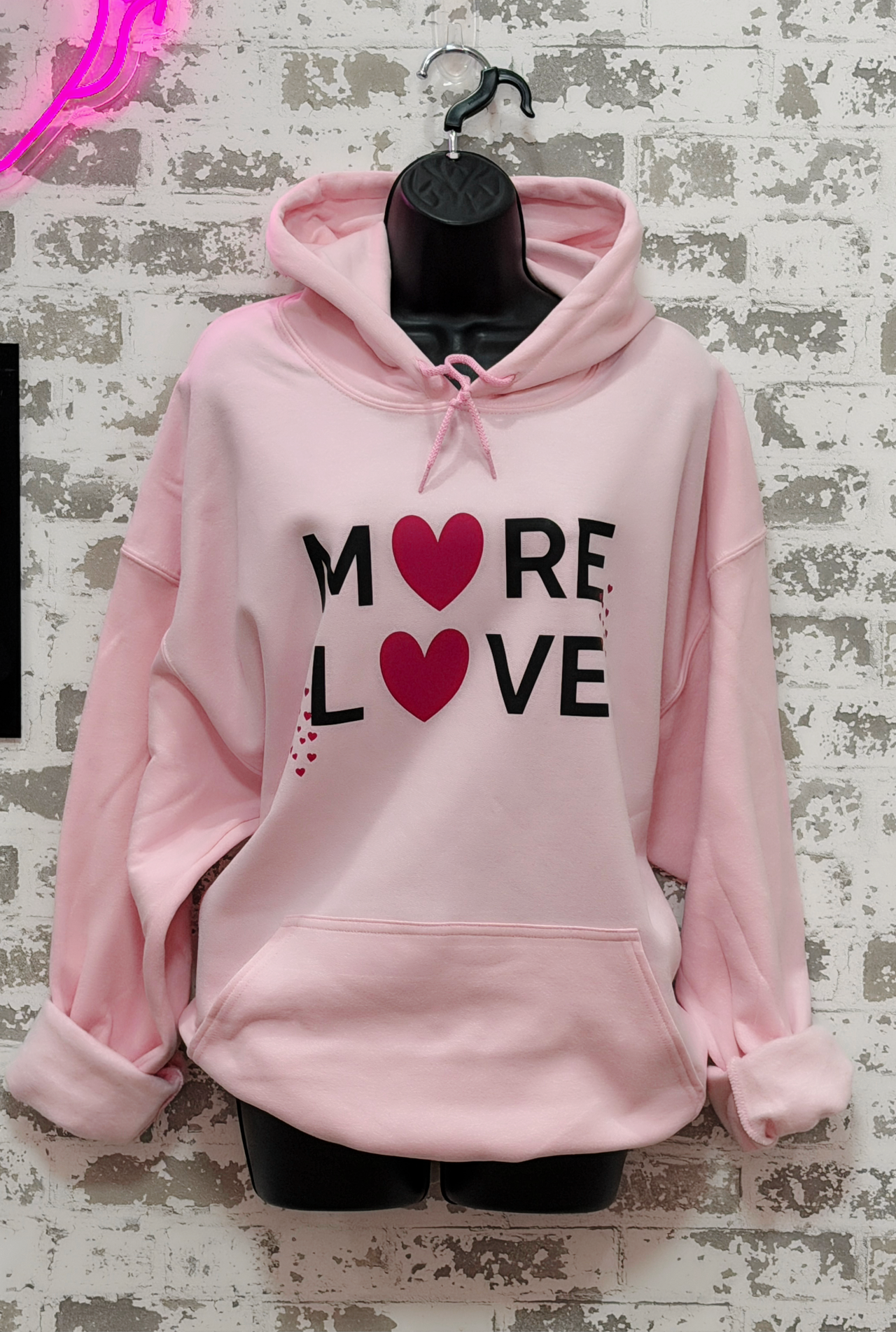 Light pink hoodie with black “MORE LOVE” lettering and pink heart graphics