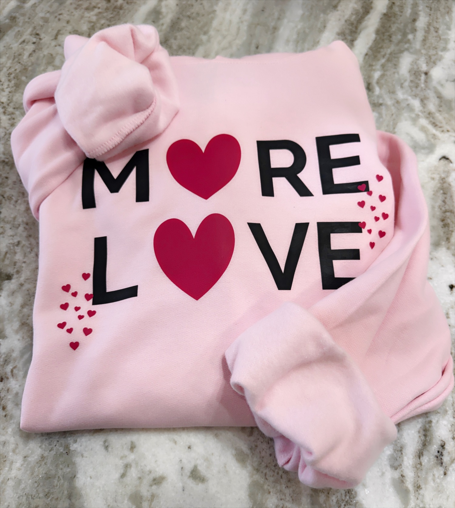 Pink hoodie with 'MORE LOVE' text and hearts on a textured surface