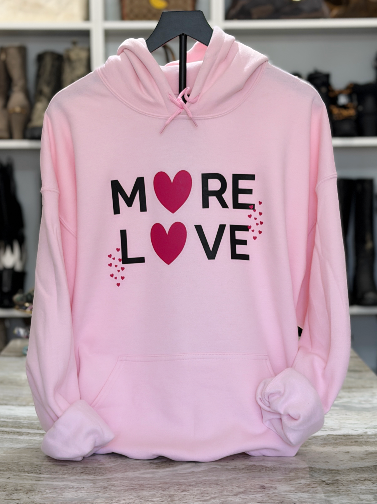 Light pink hoodie with black “MORE LOVE” lettering and pink heart graphics
