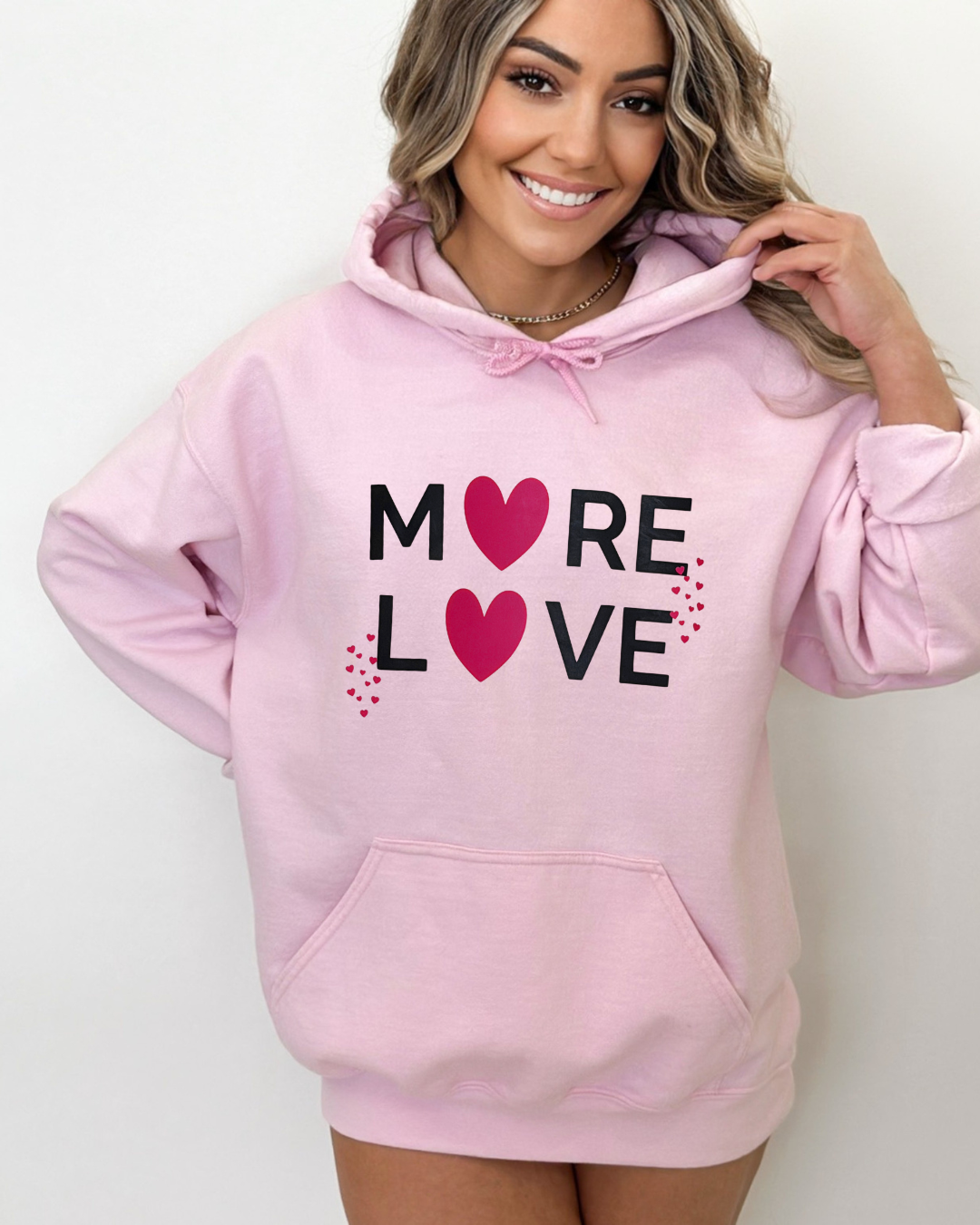 Woman wearing a pink hoodie with 'More Love' text and hearts on a white background