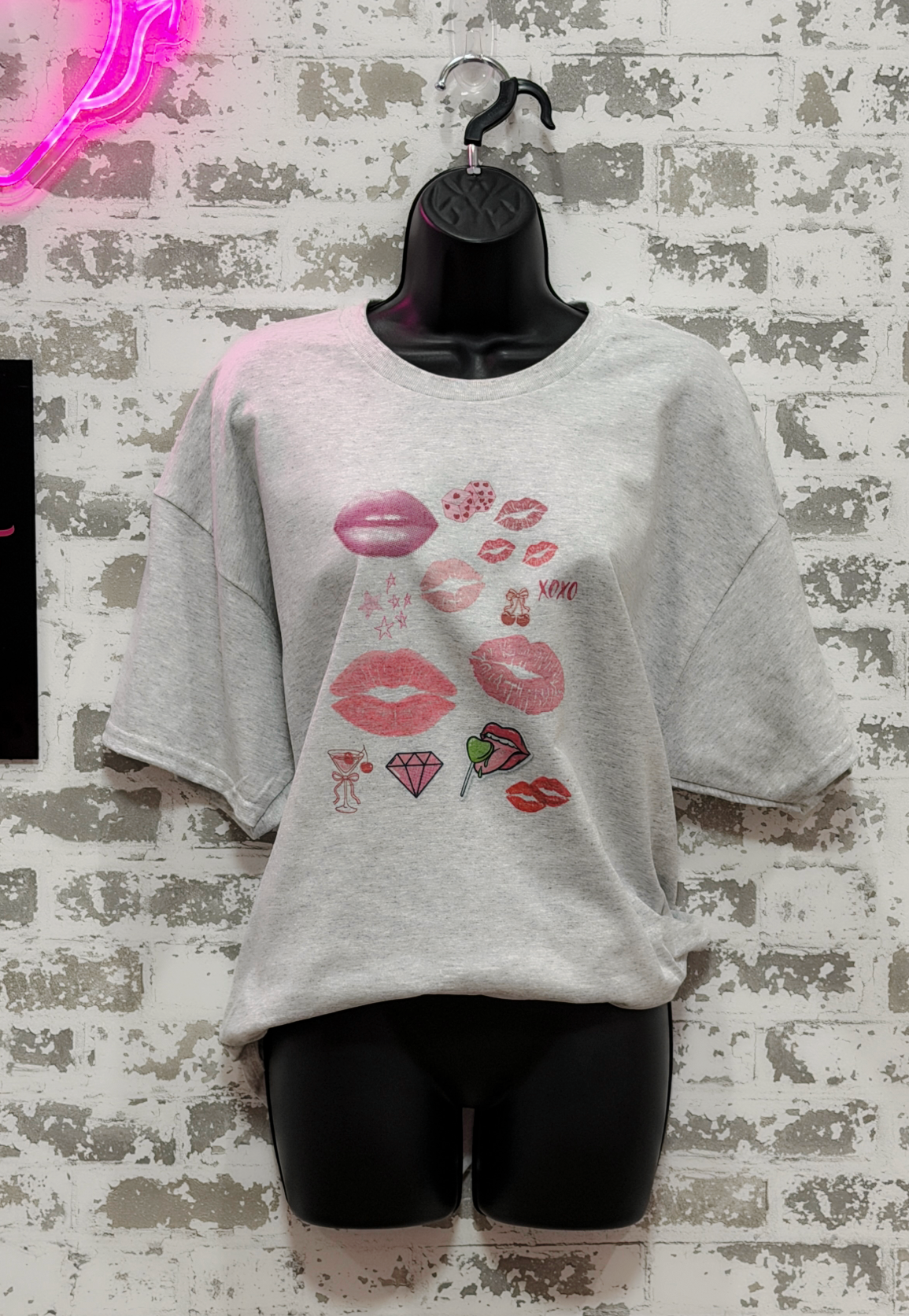 Gray oversized t-shirt with graphic designs on a mannequin against a textured wall.
