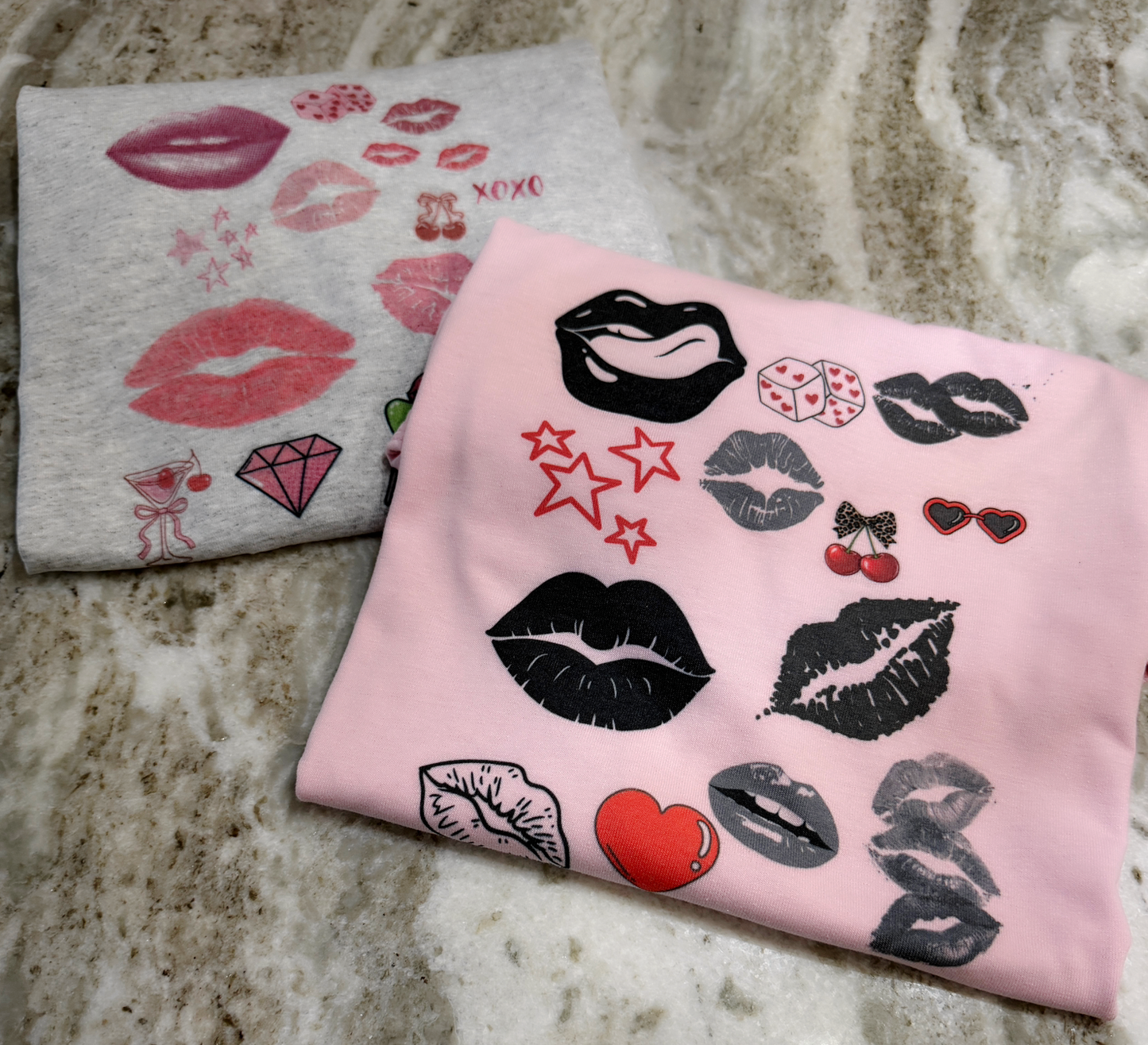 Two folded t-shirts with lip and heart designs on a marble surface