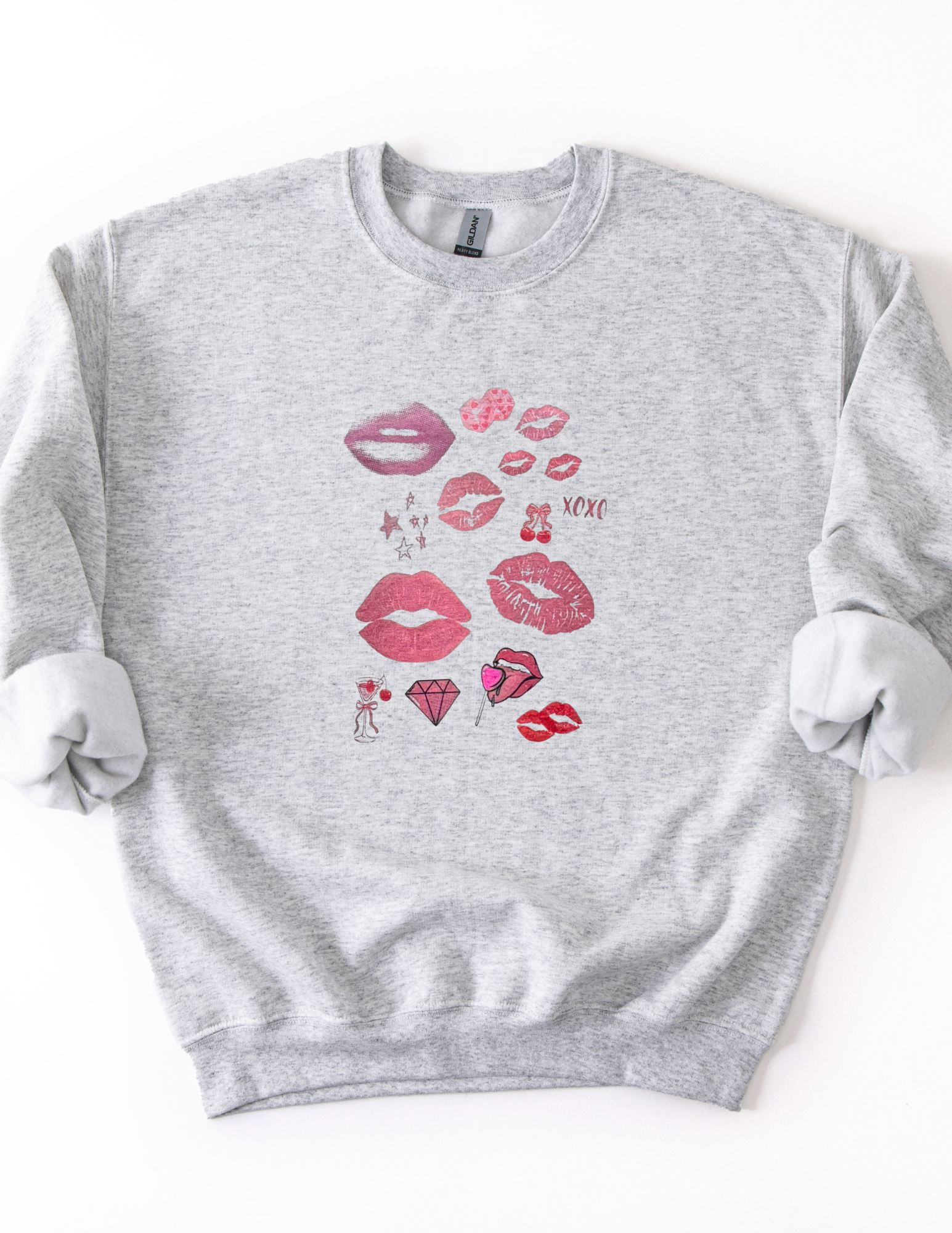 a light gray sweatshirt featuring a pop art collage of pink and red lips, stars, and playful icons from the XOXO Collection, styled casually for a relaxed, statement look.