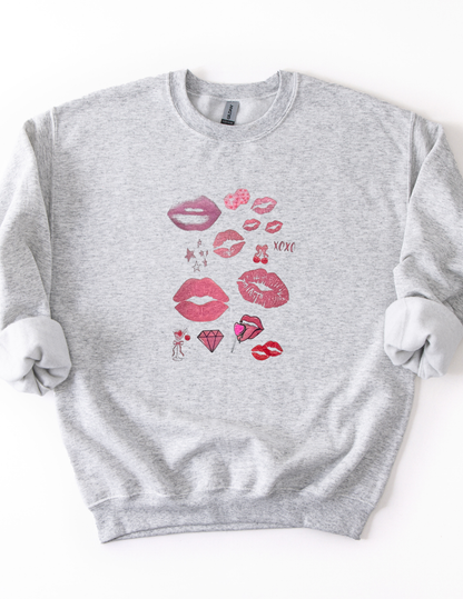 a light gray sweatshirt featuring a pop art collage of pink and red lips, stars, and playful icons from the XOXO Collection, styled casually for a relaxed, statement look.
