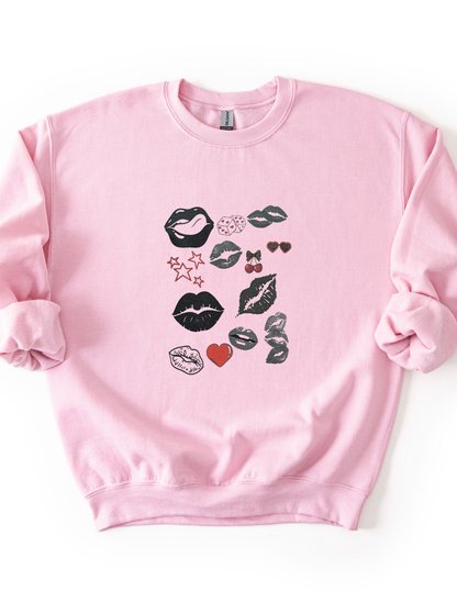 a pink sweatshirt with a bold pop art lip collage design in black and red, part of the XOXO Collection, styled for an everyday graphic statement outfit.