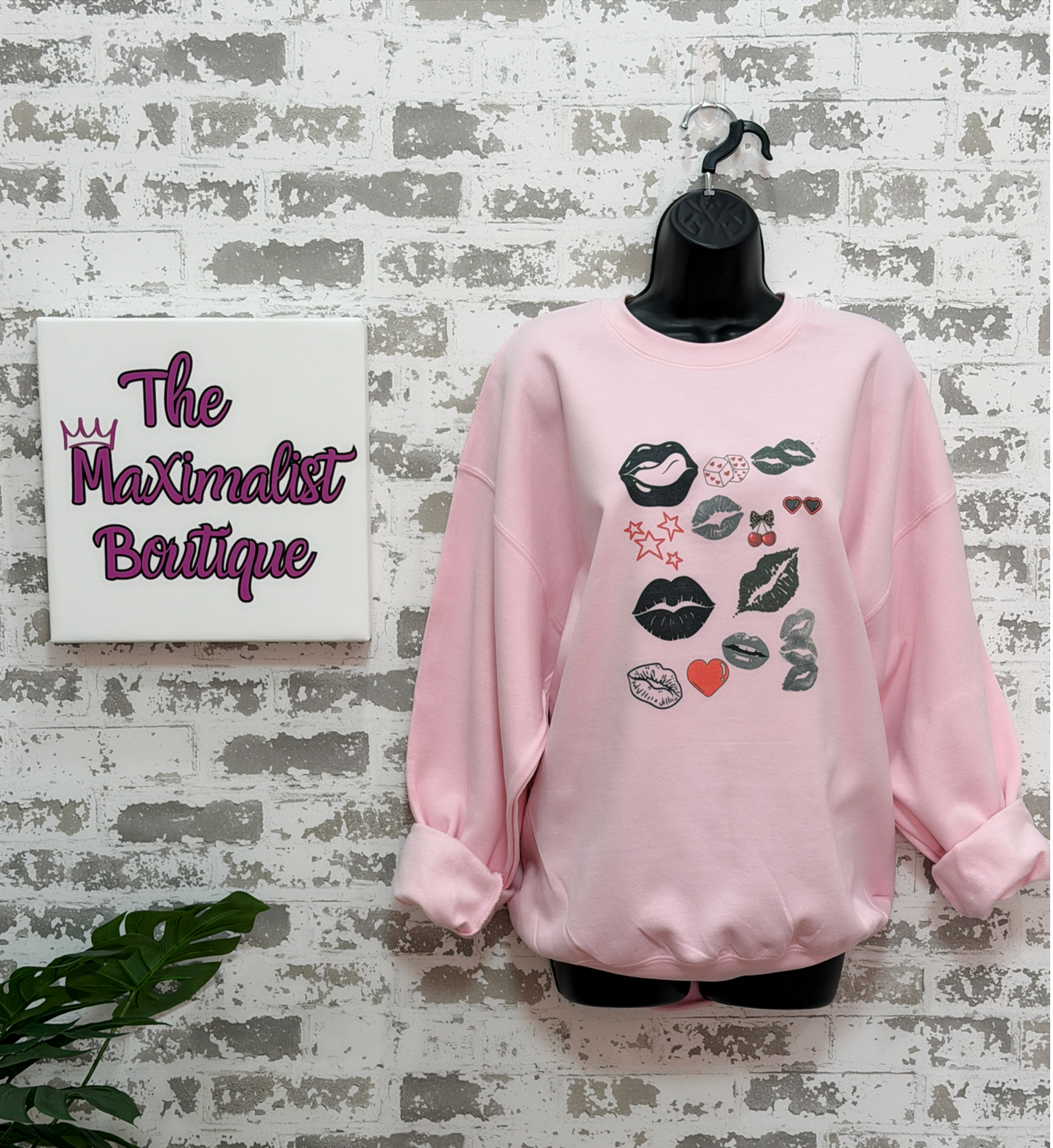 a pink sweatshirt with a bold pop art lip collage design in black and red, part of the XOXO Collection, styled for an everyday graphic statement outfit.