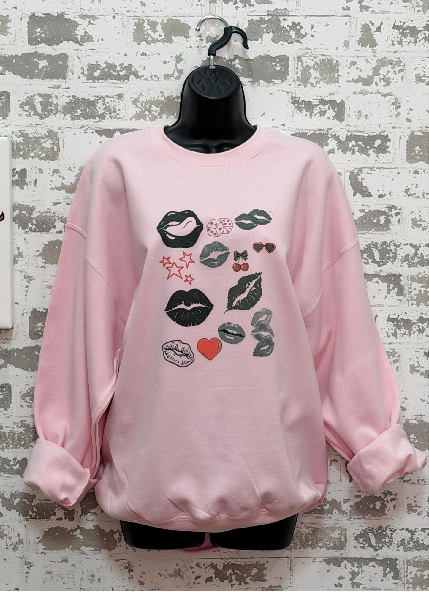 a pink sweatshirt with a bold pop art lip collage design in black and red, part of the XOXO Collection, styled for an everyday graphic statement outfit.