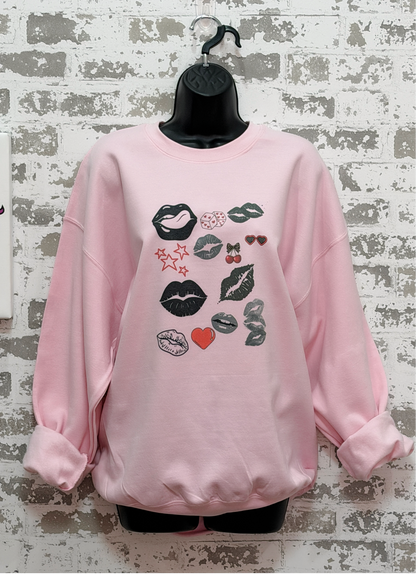a pink sweatshirt with a bold pop art lip collage design in black and red, part of the XOXO Collection, styled for an everyday graphic statement outfit.
