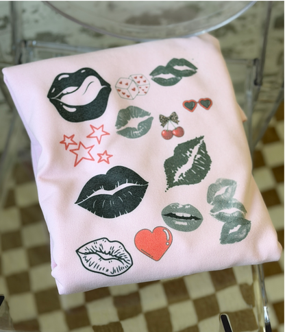 a pink sweatshirt with a bold pop art lip collage design in black and red, part of the XOXO Collection, styled for an everyday graphic statement outfit.