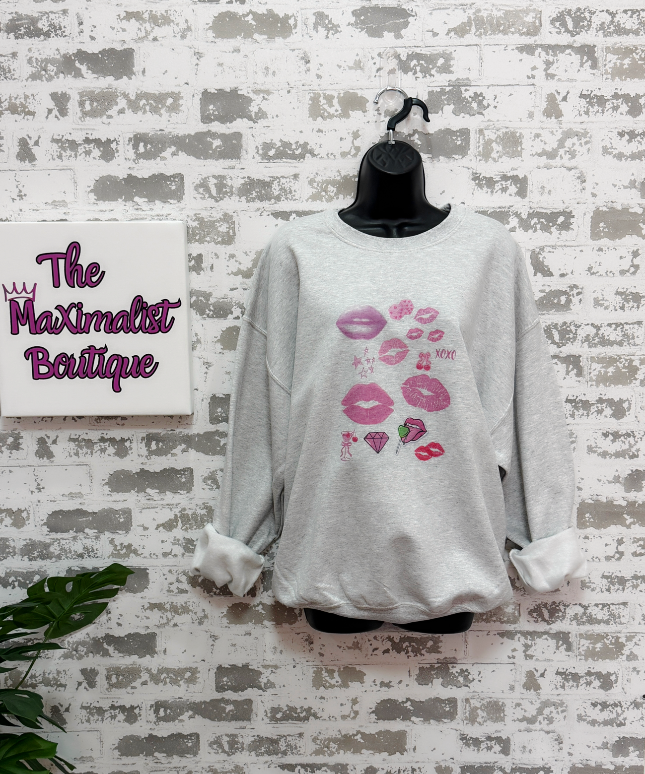 a light gray sweatshirt featuring a pop art collage of pink and red lips, stars, and playful icons from the XOXO Collection, styled casually for a relaxed, statement look.