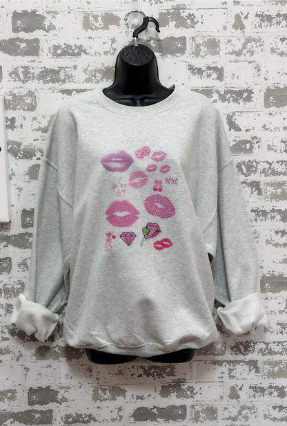 a light gray sweatshirt featuring a pop art collage of pink and red lips, stars, and playful icons from the XOXO Collection, styled casually for a relaxed, statement look.