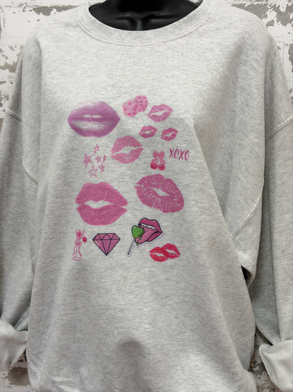 a light gray sweatshirt featuring a pop art collage of pink and red lips, stars, and playful icons from the XOXO Collection, styled casually for a relaxed, statement look.