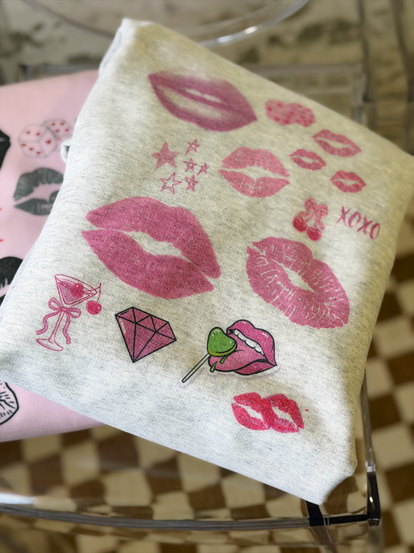 a light gray sweatshirt featuring a pop art collage of pink and red lips, stars, and playful icons from the XOXO Collection, styled casually for a relaxed, statement look.