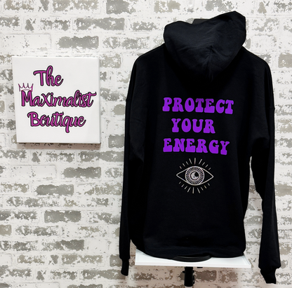 Black hoodie with purple text and an eye symbol on a textured wall background