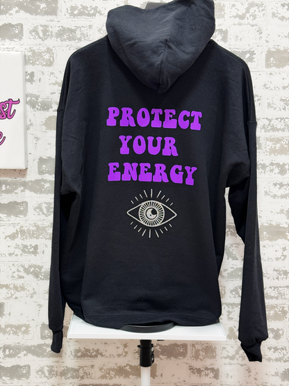 Black hoodie with 'Protect Your Energy' text and eye symbol on a brick wall background