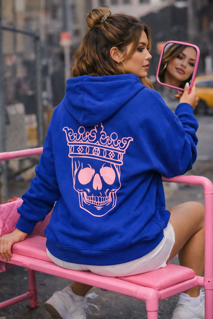 Woman wearing a blue hoodie with a pink skull design, sitting on a pink bench.