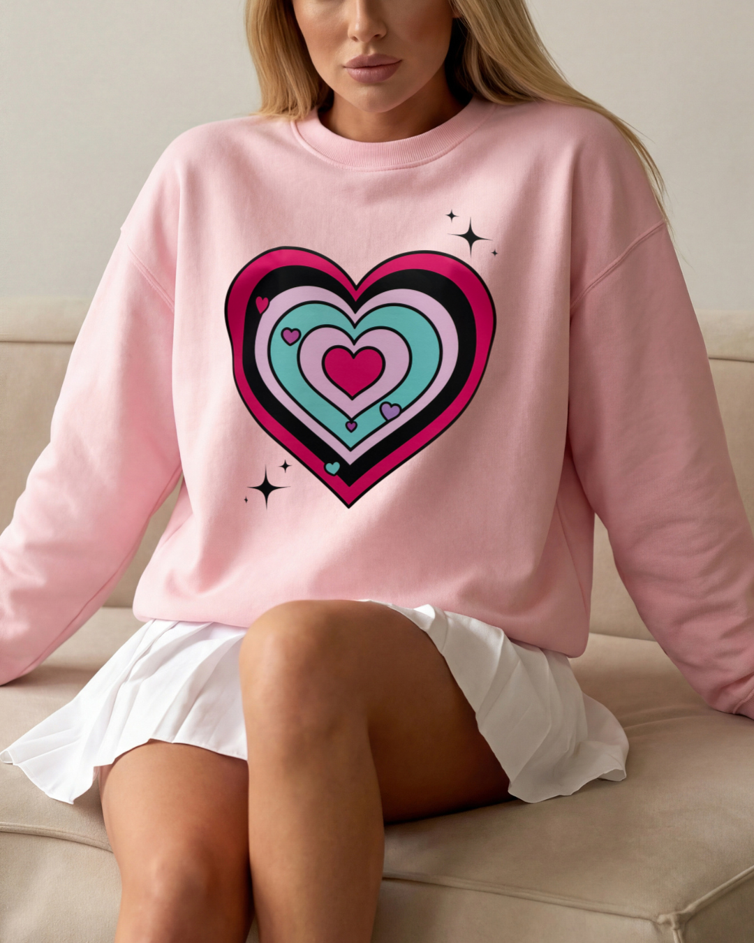 Person wearing a pink sweatshirt with a colorful heart design, sitting on a couch.