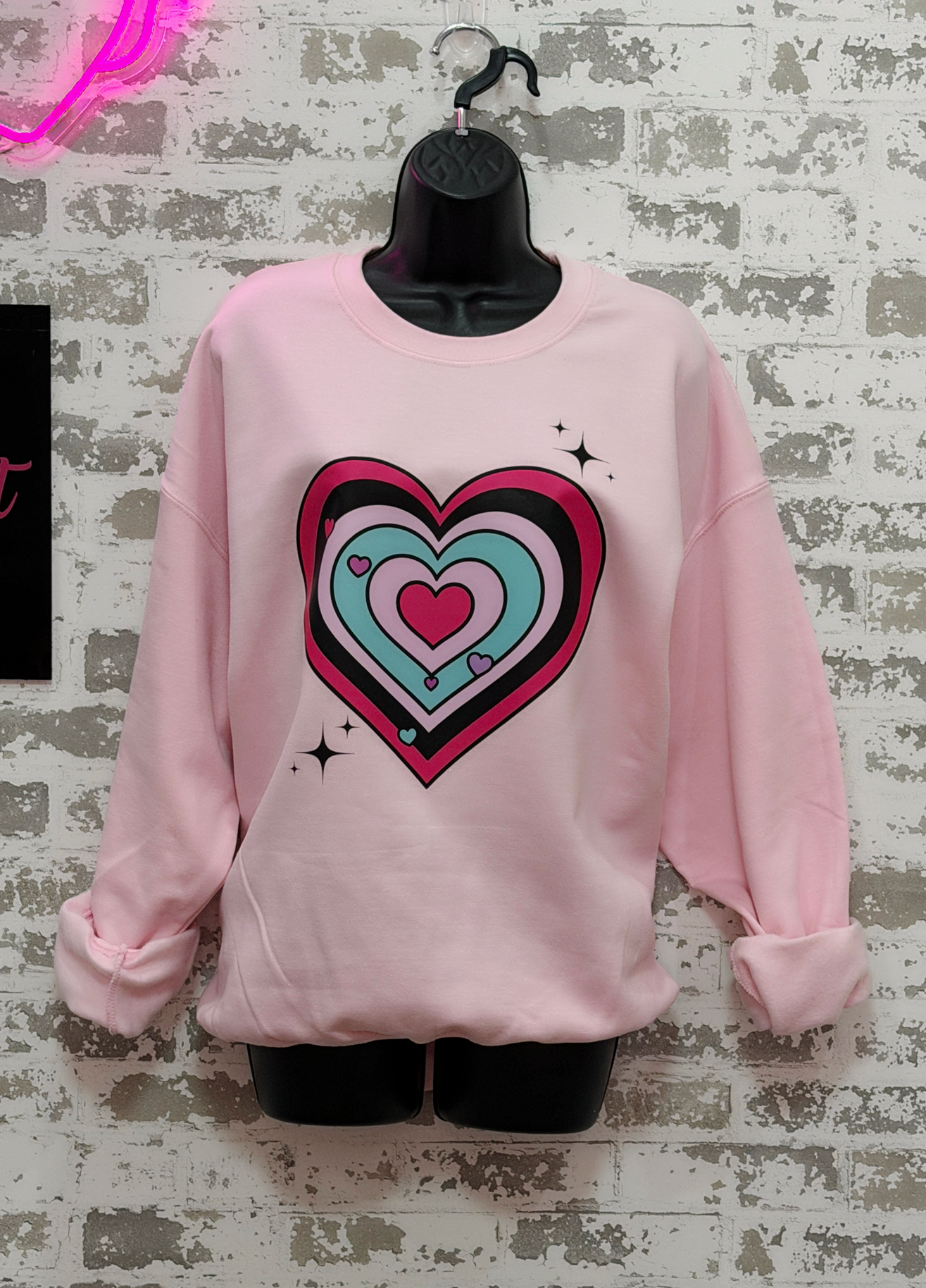 Pink sweatshirt with a colorful heart design on a textured gray background
