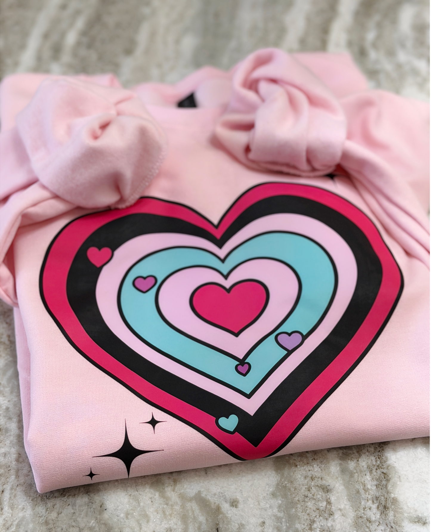 Pink sweatshirt with a colorful heart design on a textured surface